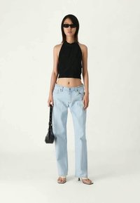 Μαύρο κοντό τζάκετ μπούστο, ανοιχτό μπλε ίσιες παντελόνες, διάφανα γυαλιά ηλίου, μαύρη τσάντα, ουδέτερο φόντο, casual παπούτσια.