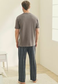 Graues T-Shirt mit kurzen Ärmeln und navyblauen, gestreiften Schlafanzughosen. Leichtes Material mit lässiger Passform. Sichtbare Streifen, die vertikal auf den Hosen verlaufen.