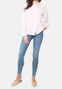 Ljusrosa skjorta med knappar och blommig brodyr, i kombination med blå skinny jeans och krämfärgade vävda mules, som har en elegant, figursydd silhuett.