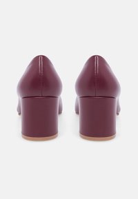 Scarpe con tacco alto in pelle bordeaux con punta arrotondata e tacco a blocco. Texture liscia, design minimalista e costruzione solida.