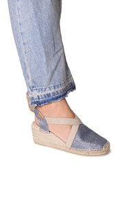 Wedge sandal with a blue and silver woven upper, beige cross-strap, and a textured jute sole. Casual design with open heel.