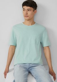 Lichtblauw T-shirt met korte mouwen, ronde hals en een borstzak, gemaakt van zachte stof, gecombineerd met lichtblauwe jeans.