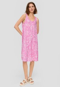 Rosa ärmelloses Kleid mit einem weißen Blumenmuster, lockerer Schnitt, knielang. Kombiniert mit beigen Plateausandalen. Glattes, leichtes Material.