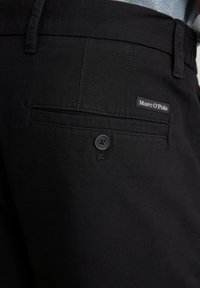 Schwarze Stoffhose mit einer Gesäßtasche und Knopfverschluss sowie einem Etikett mit der Aufschrift "Marc O'Polo". Glatte Textur mit schlichten Design.