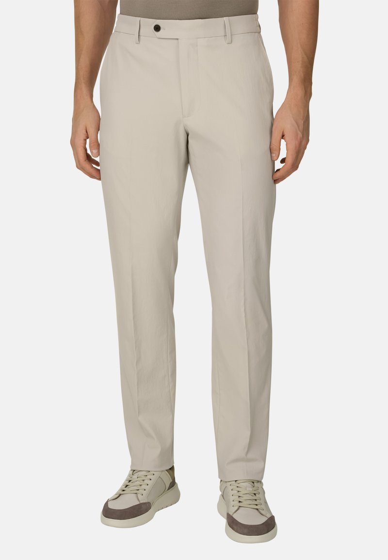Pantalon beige clair avec une texture lisse, coupe ajustée, poches avant et fermeture à bouton unique, associé à des baskets claires.