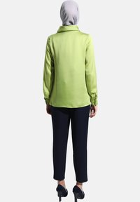 Grüne Satinbluse mit langen Ärmeln und einem Kragen, kombiniert mit marineblauen Hosen und hohen Schuhen. Die Bluse hat eine glatte Textur und eine lockere Passform.