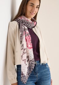 Sciarpa leggera e decorata in tonalità di rosa, grigio e bianco con motivo leopardato. Indossata drappeggiata attorno al collo sopra un top aderente.