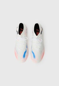 Weiße Sportschuhe mit einem gemusterten Strick-Obermaterial, ausgestattet mit blauen und rosa Akzenten, flachen weißen Schnürsenkeln und einem schwarzen Logo an der Ferse.