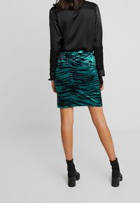 Sammet mini kjol i teal med svarta tigerstrimmor, kombinerat med en svart satin långärmad skjorta och svarta klackiga ankelstövlar.