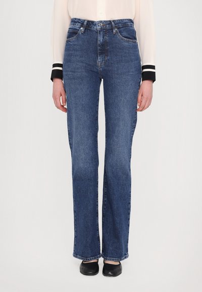 Pantalon en denim bleu foncé avec une taille haute, coupe droite et coutures visibles. Comprend des poches et des passants de ceinture.