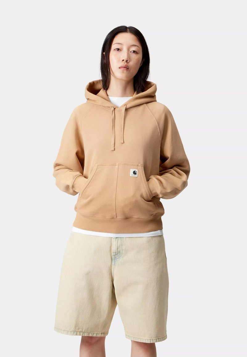 Sudadera marrón clara con un bolsillo tipo canguro, capucha con cordón y puños acanalados. Combinada con pantalones cortos beige. Textura suave, diseño casual.
