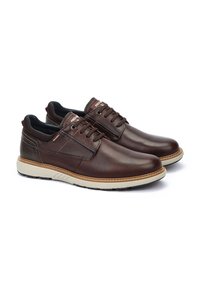 Zapatos de cuero marrón con textura suave, diseño de cordones y suela de goma clara en contraste. Presenta costuras y sutiles acentos de marca.