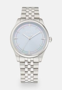 Montre en acier inoxydable argenté avec un cadran bleu clair, présentant de fines aiguilles argentées, un sous-cadran simple et un bracelet en métal poli.