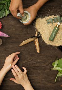Mortier et pilon avec des contents verts, une bouteille cosmétique verte, des bâtons en bois, des feuilles d'aloe vera et des grains texturés sur une surface en bois sombre.