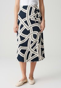 Jupe enveloppante bleu marine avec un motif de rayures abstraites crème, longueur mi-mollet, tissu léger, lien à la taille, complétée par des chaussures claires.