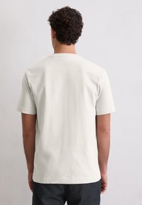 Hellbeiges T-Shirt aus Baumwolle mit kurzen Ärmeln. Rundhalsausschnitt und lockere Passform. Glatte Textur ohne sichtbare Muster oder Grafiken.