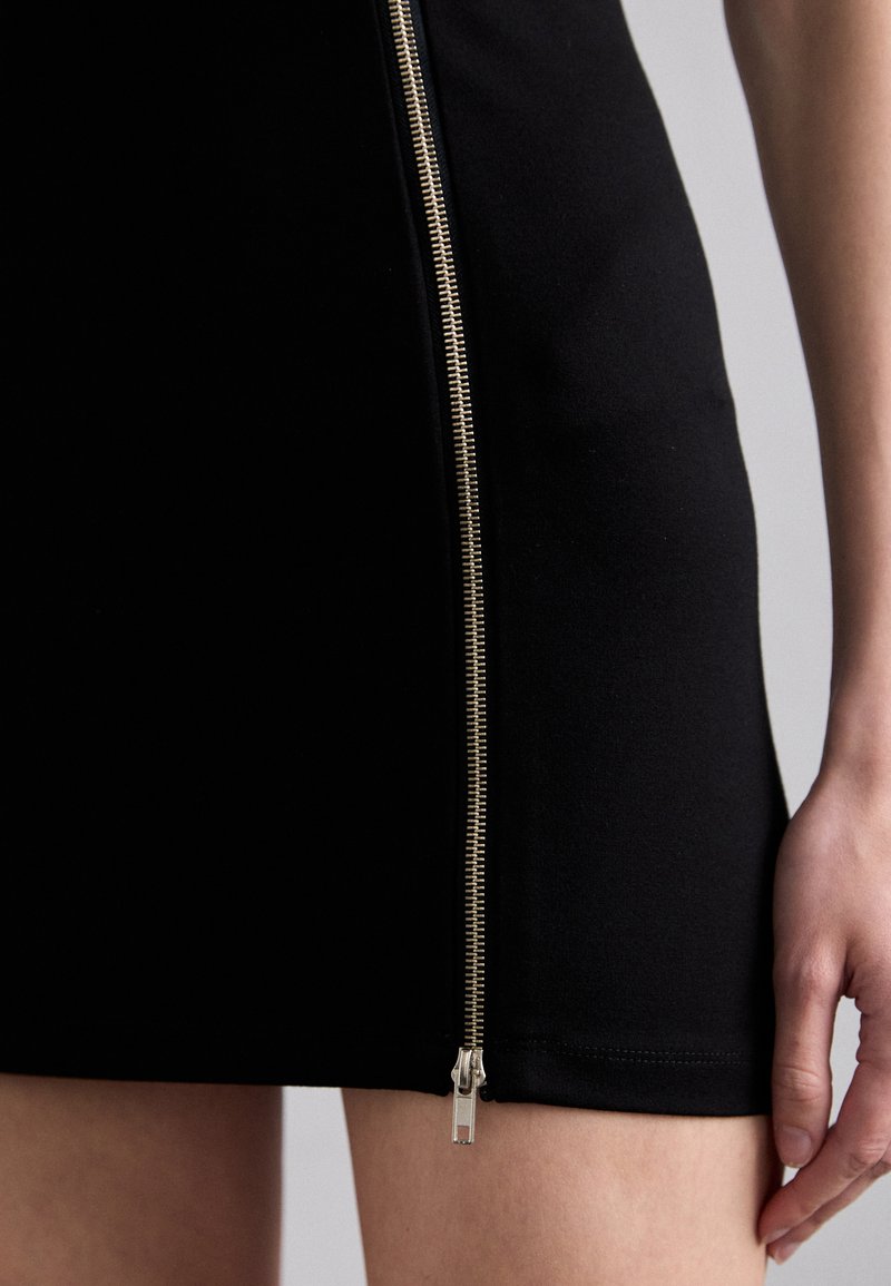 Vestito nero con una silhouette aderente, presenta una cerniera laterale dorata, una texture liscia e un orlo sopra la metà della coscia.