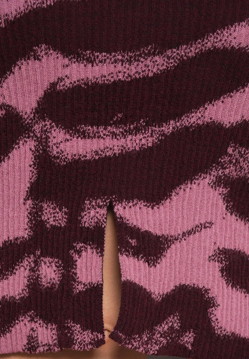 Strickstoff mit einem burgunderfarbenen und rosa Muster, das einem Tierstreifen ähnelt, und einem kleinen Schlitzdetail. Weiche Textur, mittleres Gewicht.
