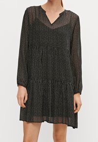 Robe noire à fines rayures blanches verticales, encolure en V, manches longues, corsage froncé et jupe à volants. Matière transparente avec une texture légère.