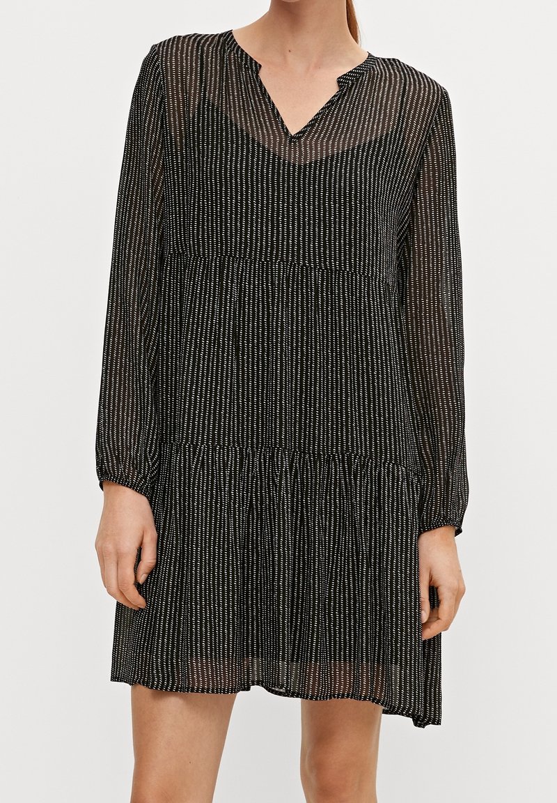 Robe noire à fines rayures blanches verticales, encolure en V, manches longues, corsage froncé et jupe à volants. Matière transparente avec une texture légère.