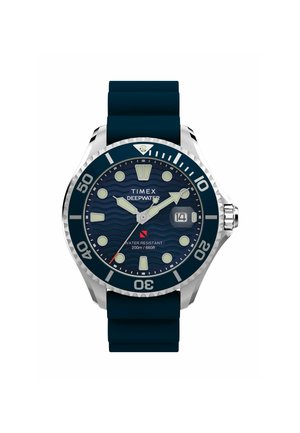 Montre Timex Deepwater avec un boîtier en acier inoxydable, un bracelet en caoutchouc bleu marine, un cadran à motif de vagues, des marqueurs lumineux et une fenêtre de date. Étanche jusqu'à 200 m.