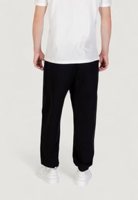 Zwarte joggingsbroek met een ontspannen pasvorm, gemaakt van zachte stof, met elastische boorden en een verstelbare tailleband, gecombineerd met witte sneakers.
