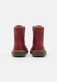 Botas de tobillo de cuero rojo con un acabado suave, cremalleras laterales y suelas de goma marrón texturizadas. Acentos de costura a lo largo de la suela.