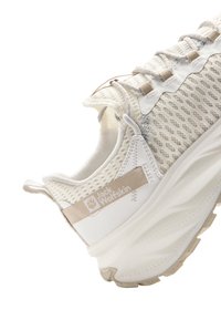 Sneaker légère avec une tige en mesh dans des teintes crème et beige, dotée d'un col rembourré, d'une semelle texturée et d'un logo imprimé sur le côté.
