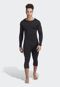 Black long-sleeve thermal top and 3/4-length leggings, made of smooth fabric with a fitted design and minimal seams, barefoot on a plain background.