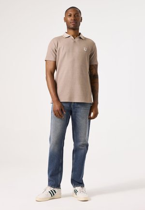 Camisa polo beige con cuello, mangas cortas y un pequeño logotipo; combinada con jeans azul claros y zapatillas blancas con rayas verdes.