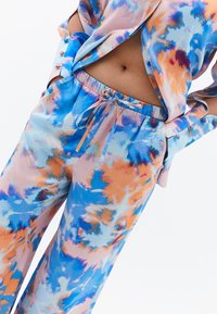Ensemble fluide et multicolore en tissu léger ; présente un motif tie-dye en bleu, orange et rose, avec une taille élastique et des manches boutonnées.