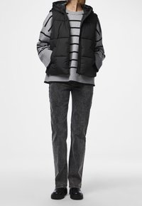 Svart vadderad väst med huva över en grårandig tröja, matchad med mörkgrå jeans och svarta skor.