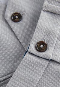 Gros plan sur un tissu gris clair texturé avec deux boutons marron foncé gravés de "Baker Baker."