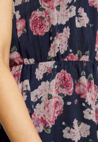 Blommig klänning med marinblå bakgrund, prydd med stora rosa rosor. Tillverkad av lätt, texturerad tyg med en samlad midja.