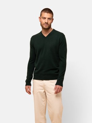 Donkergroen v-hals sweater van zacht materiaal, met lange mouwen en een getailleerde silouette, gecombineerd met lichtbeige broek.