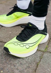 Shoe de corrida amarelo neon com detalhes em preto, parte superior texturizada e sola branca. Apresenta um design elegante e cinco linhas circulares de detalhes.