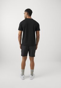 Svart t-skjorte med korte ermer, kombinert med mørke treningsshorts. Enkelt design, myk tekstur. Fottøy: hvite joggesko med grå sokker.