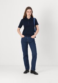 Marineblå polo shirt med korte ærmer, tre-knap lukning, kombinert med mørke denim jeans og svarte sko. Enkelt og tilpasset design.