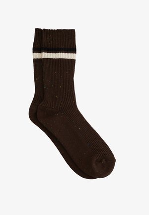 Calcetines marrones de canalé con manchas multicolores, con un puño a rayas en blanco y negro. Textura suave, longitud hasta la mitad de la pantorrilla y punta redondeada.