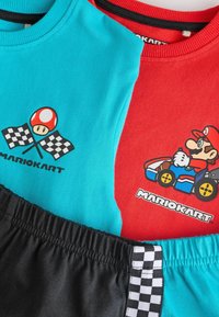 Dos camisas de algodón: una turquesa con un hongo y banderas, y una roja con un diseño de Mario Kart. Un pantalón corto negro con un acento de cuadros.