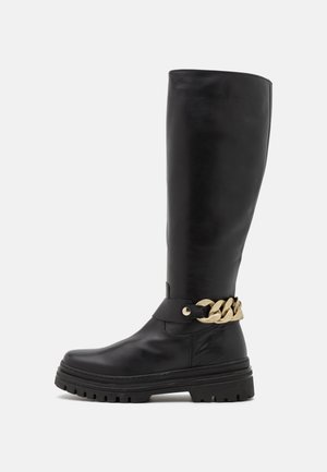 Bottes hautes en cuir noir avec une semelle épaisse, ornées d'un accent de chaîne dorée autour de la cheville et une texture lisse.