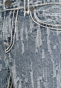 Jeans de mezclilla azul con textura desgastada, con costuras blancas y botón metálico. Desvanecimientos sutiles y acentos deshilachados en la tela.