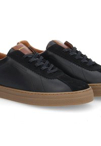 Zapatillas de cuero negro con acentos de ante marrón, suela gruesa de goma cruda y cordones negros. Presentan un acabado suave y un panel lateral texturizado.