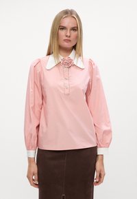 Blusa rosa con maniche a sbuffo, colletto bianco e dettaglio a rosa, chiusura frontale con bottoni, texture liscia, progettata con sottili decorazioni.