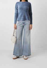 Blauer strukturierter Pullover, helle, weit geschnittene Jeans in Blau, weiße Tasche mit Kettenhenkel und weiße Sneakers mit Gummisohlen.