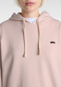 Lyserød hoodie lavet af blødt stof, med en kængurulomme og justerbare snore, samt et lille sort skateboard-logo broderet.