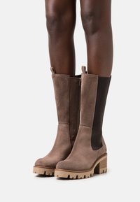 Bottes cheville en daim marron avec talon bloc, dotées de panneaux latéraux élastiques et d'une fermeture éclair, finition texturée, et semelle en caoutchouc solide.
