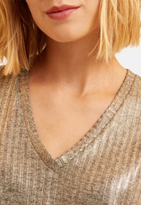 Top en tricot métallisé doré avec une texture côtelée, présentant un décolleté en V profond et des manches courtes, rehaussé d'une finition scintillante.