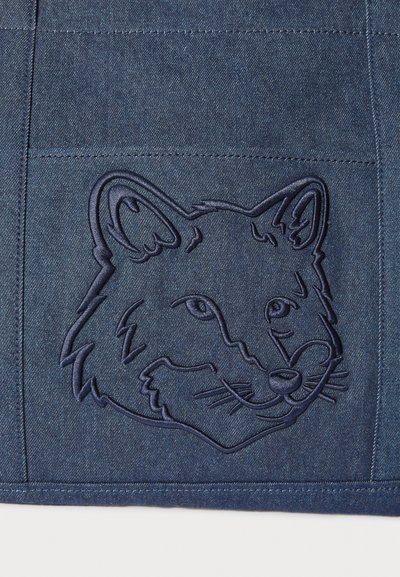 Σκούρο μπλε τζιν ύφασμα με ανάγλυφο σχέδιο κεφαλιού αλεπούς. Η περίπλοκη λεπτομέρεια αναδεικνύει τα χαρακτηριστικά του προσώπου με υφή φινιρίσματος.