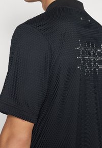 Polo shirt nero a maniche corte con un design in mesh testurizzato, colletto a coste e cuciture decorative sul retro.